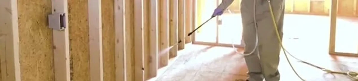 Termite treatment technician applying spray along framing and unfinished walls in Pembroke PInes, FL